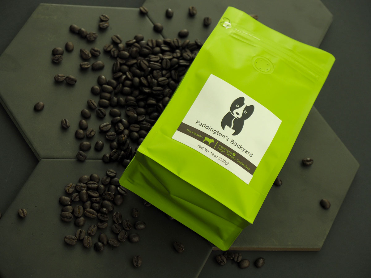 top-view of franklin dark roast coffee bag with roasted beans scattered around a noir backdrop